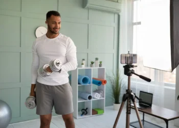 Homem treinando em jejum com halteres enquanto grava seu treino em ambiente caseiro.