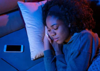 Mulher dormindo em ambiente escuro com celular ao lado