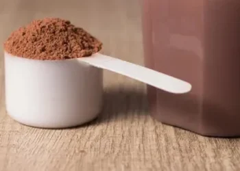 Medidor com whey protein e shake pronto sobre mesa de madeira