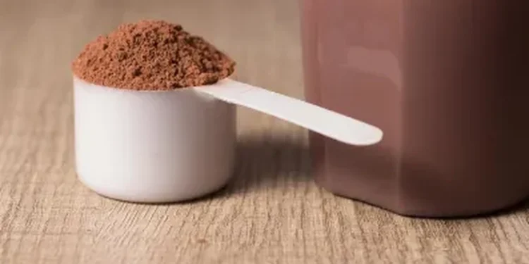 Medidor com whey protein e shake pronto sobre mesa de madeira