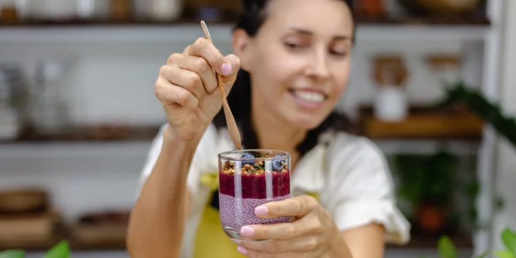 Mulher segurando copo com pudim de chia, frutas vermelhas e granola