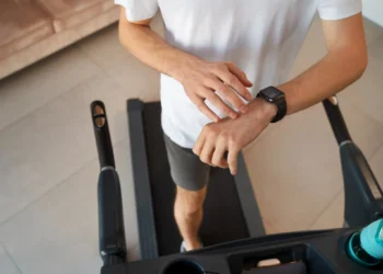 Homem ajustando o relógio de treino enquanto caminha em esteira dentro de casa