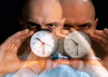 Relógios sendo segurados por homem, com uma expressão intensa, representando o conceito de relógio biológico e sua influência na saúde humana.