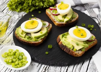 Sanduíche de pão integral com abacate, ovo cozido e cebolinhas frescas, ideal para uma refeição simples e nutritiva.