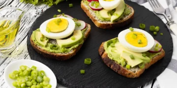 Sanduíche de pão integral com abacate, ovo cozido e cebolinhas frescas, ideal para uma refeição simples e nutritiva.