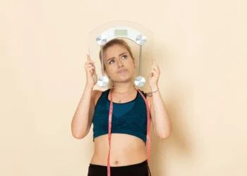 Mulher jovem com roupa esportiva segurando uma balança, refletindo sobre o impacto da saúde mental no emagrecimento.
