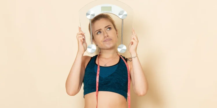 Mulher jovem com roupa esportiva segurando uma balança, refletindo sobre o impacto da saúde mental no emagrecimento.