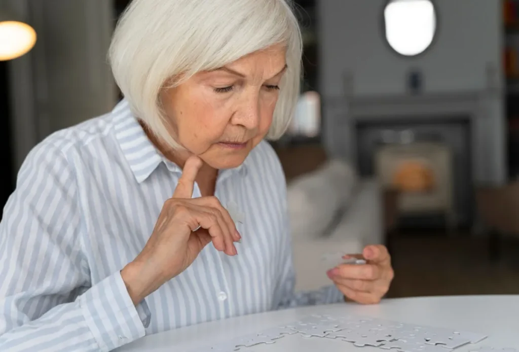 Mulher idosa concentrada montando quebra-cabeça, representando os desafios cognitivos do Alzheimer.