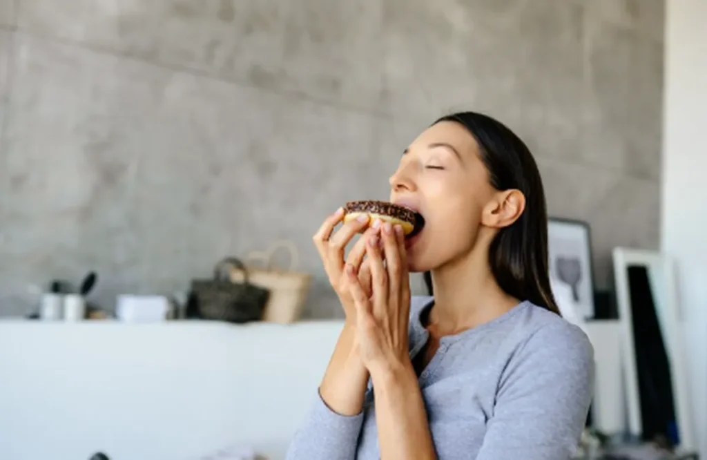 Mulher comendo um donut, ilustrando os sintomas de abstinência ao parar de consumir açúcar.