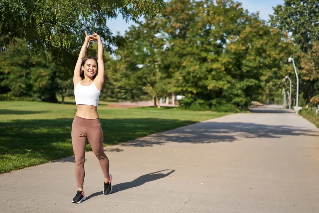 Mulher se alongando após treino da tarde em parque com clima ensolarado