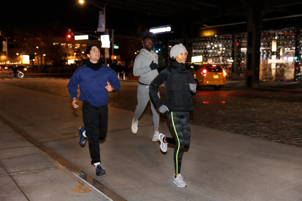 Três amigos correndo juntos à noite em uma rua iluminada da cidade