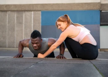 Homem fazendo flexão ao ar livre com a ajuda de uma mulher durante treino para ganho de músculos e definição corporal.