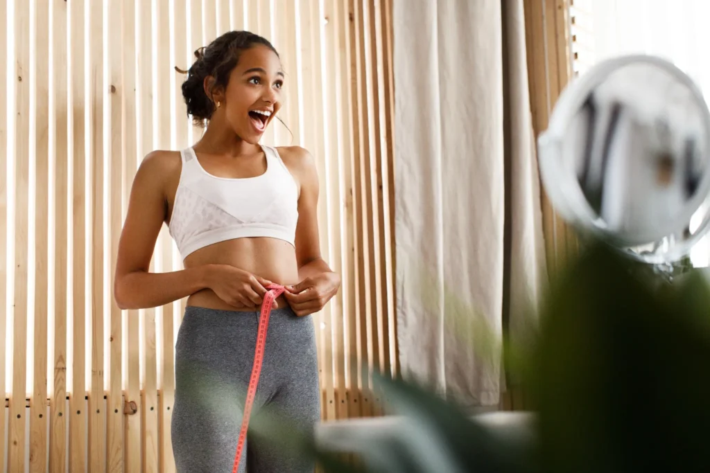 Mulher medindo sua cintura, visivelmente feliz com os resultados do treino em jejum.