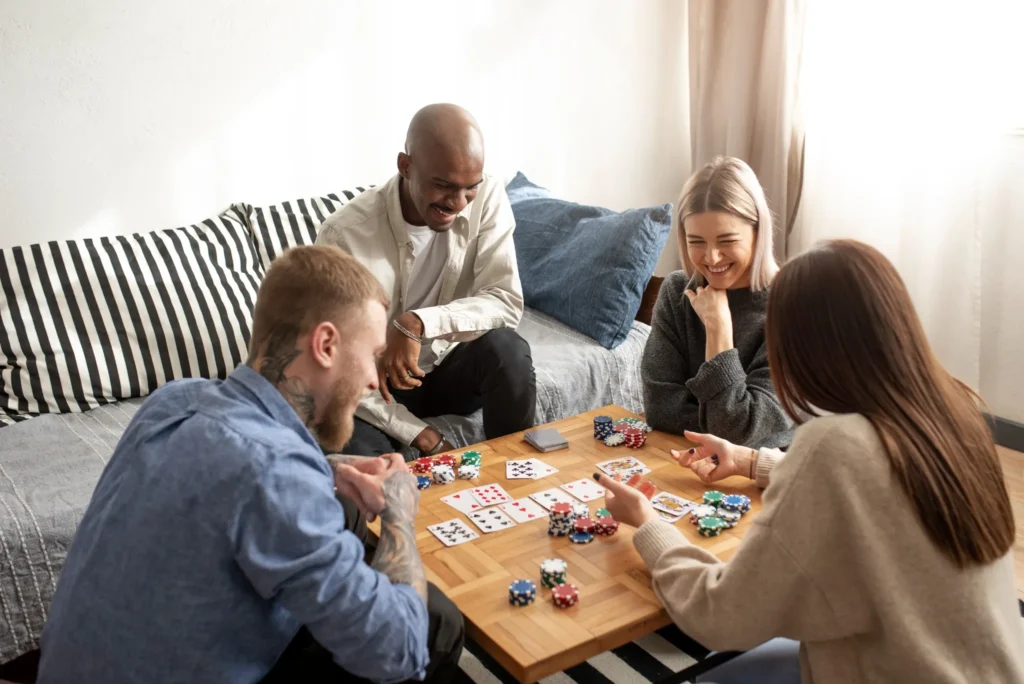 Grupo de amigos se divertindo enquanto jogam poker, com fichas e cartas sobre a mesa.