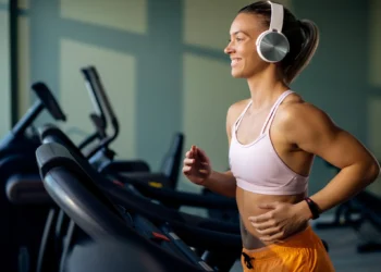 Mulher correndo feliz em uma esteira de academia com fones de ouvido, focada em seus treinos.