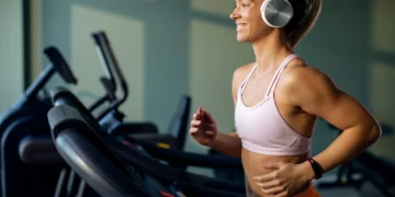 Mulher correndo feliz em uma esteira de academia com fones de ouvido, focada em seus treinos.