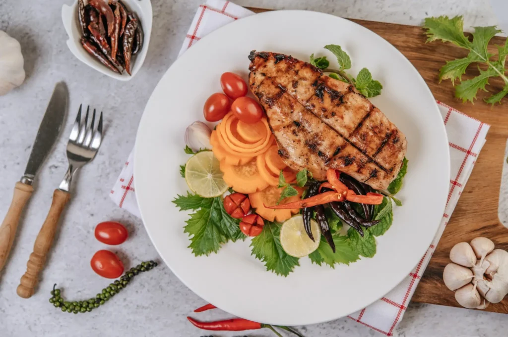 Prato saudável com peito de frango grelhado, cenoura, tomate, pimentão e folhas frescas.