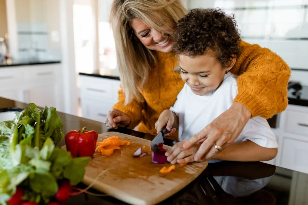 Criança e adulto cortando legumes juntos em uma cozinha moderna.