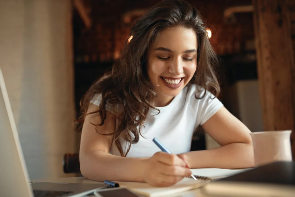 Mulher sorrindo enquanto escreve em um caderno, cultivando o aprendizado contínuo