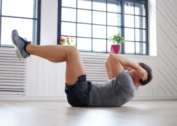 Homem realizando exercício abdominal em casa, ajudando a reduzir a barriguinha com atividade física.