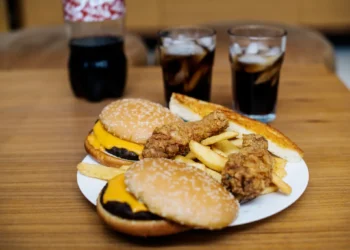 Imagem de junk food com hambúrgueres, batatas fritas, frango frito e refrigerante, que ilustram alimentos que podem causar inchaço mesmo em pequenas quantidades.