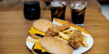 Imagem de junk food com hambúrgueres, batatas fritas, frango frito e refrigerante, que ilustram alimentos que podem causar inchaço mesmo em pequenas quantidades.