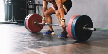 Pessoa realizando levantamento terra, um exercício de força com barra, focando na postura correta e técnica de levantamento.