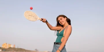 Mulher se divertindo jogando Beach Tennis na praia, usando raquete e bola