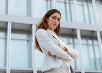 Mulher poderosa de negócios em pose confiante, com expressão de autoestima elevada em frente a um edifício moderno.