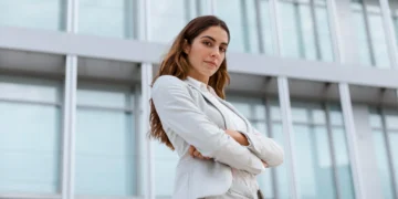 Mulher poderosa de negócios em pose confiante, com expressão de autoestima elevada em frente a um edifício moderno.