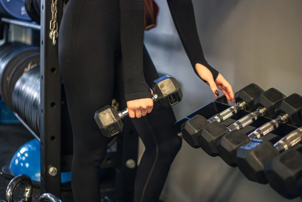 Mulher jovem no ginásio levantando halteres, realizando exercícios com técnica correta para progressão de carga