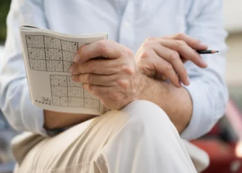 Homem resolvendo um Sudoku em papel, desafiando a mente com exercícios mentais.