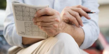 Homem resolvendo um Sudoku em papel, desafiando a mente com exercícios mentais.