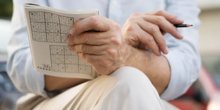 Homem resolvendo um Sudoku em papel, desafiando a mente com exercícios mentais.