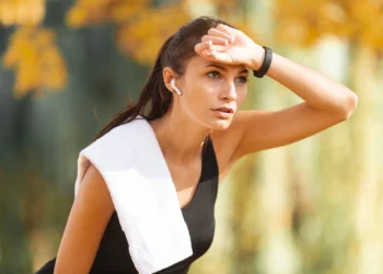 Mulher suada, vestindo roupas de treino, se exercitando ao ar livre em um ambiente de calor intenso.