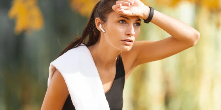 Mulher suada, vestindo roupas de treino, se exercitando ao ar livre em um ambiente de calor intenso.