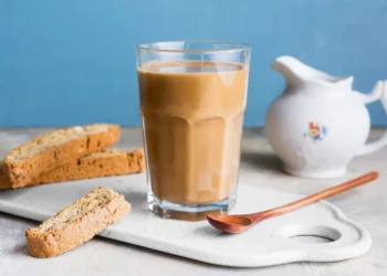 Café com leite servido em copo transparente, acompanhado de fatias de biscoito crocante