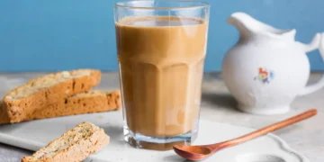 Café com leite servido em copo transparente, acompanhado de fatias de biscoito crocante
