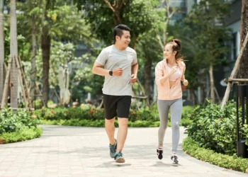 Casal praticando caminhada ao ar livre, uma tendência fitness japonesa, sorrindo e se exercitando juntos no parque.