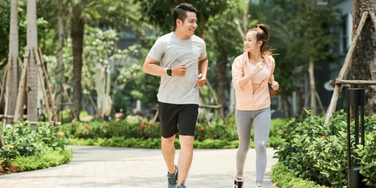 Casal praticando caminhada ao ar livre, uma tendência fitness japonesa, sorrindo e se exercitando juntos no parque.