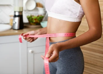 Mulher medindo a cintura com fita métrica, representando o acompanhamento do emagrecimento através de esportes eficazes na queima calórica.