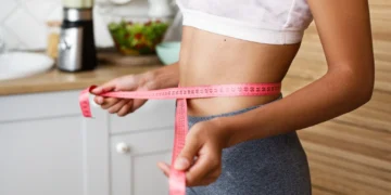 Mulher medindo a cintura com fita métrica, representando o acompanhamento do emagrecimento através de esportes eficazes na queima calórica.