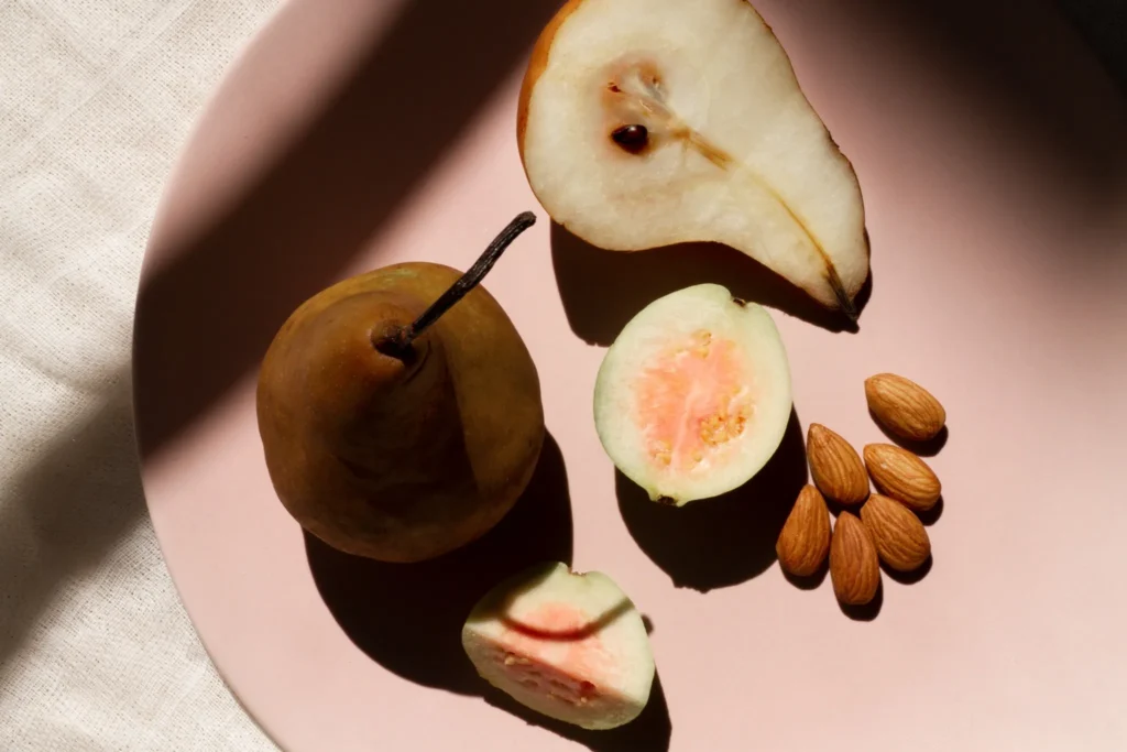Fruta fatiada, incluindo pera e goiaba, acompanhada de amêndoas.