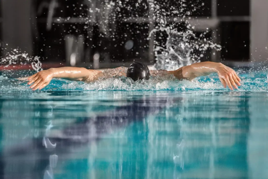 Nadador masculino executando o estilo borboleta na piscina, destacando a técnica de movimento dos braços.
