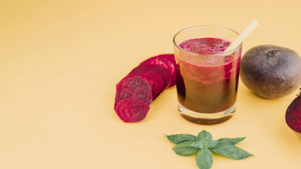 Suco de beterraba fresco em copo com fatias de beterraba ao lado, sobre fundo amarelo