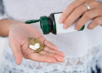 Mulher derramando cápsulas de suplemento da garrafa em sua mão.