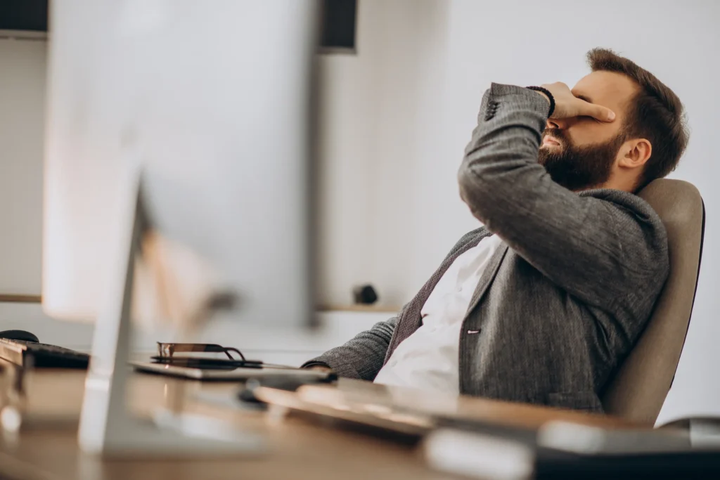 Homem cansado cobrindo o rosto com a mão devido ao estresse no trabalho.