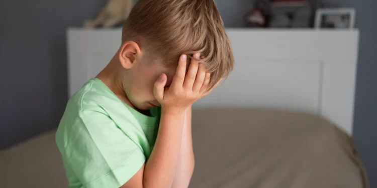 Criança com expressão de tristeza cobrindo o rosto, possível sinal de ansiedade infantil