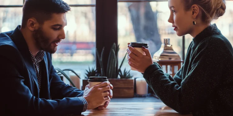 Homem desviando o olhar enquanto conversa com uma mulher em um café, revelando possível desconforto ou desinteresse.