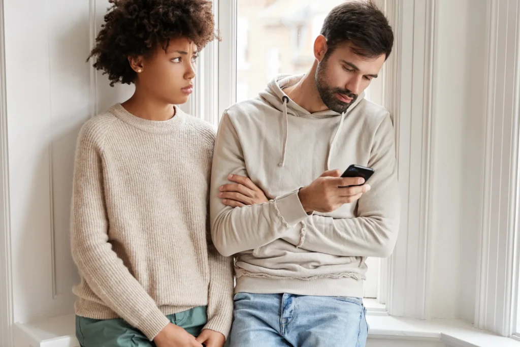 Casal em silêncio, com um dos parceiros distraído no celular enquanto o outro parece distante, simbolizando a falta de comunicação e o fim de um relacionamento.